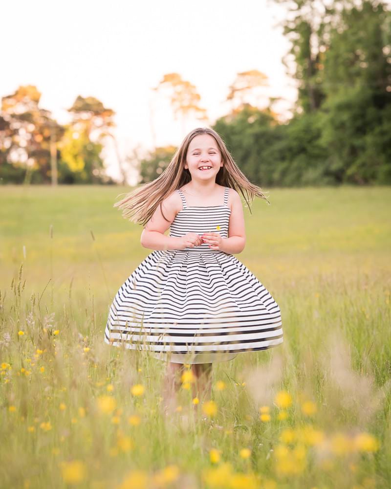 A young girl dancing in a buttercup meadow during her family photoshoot in Ardingly
