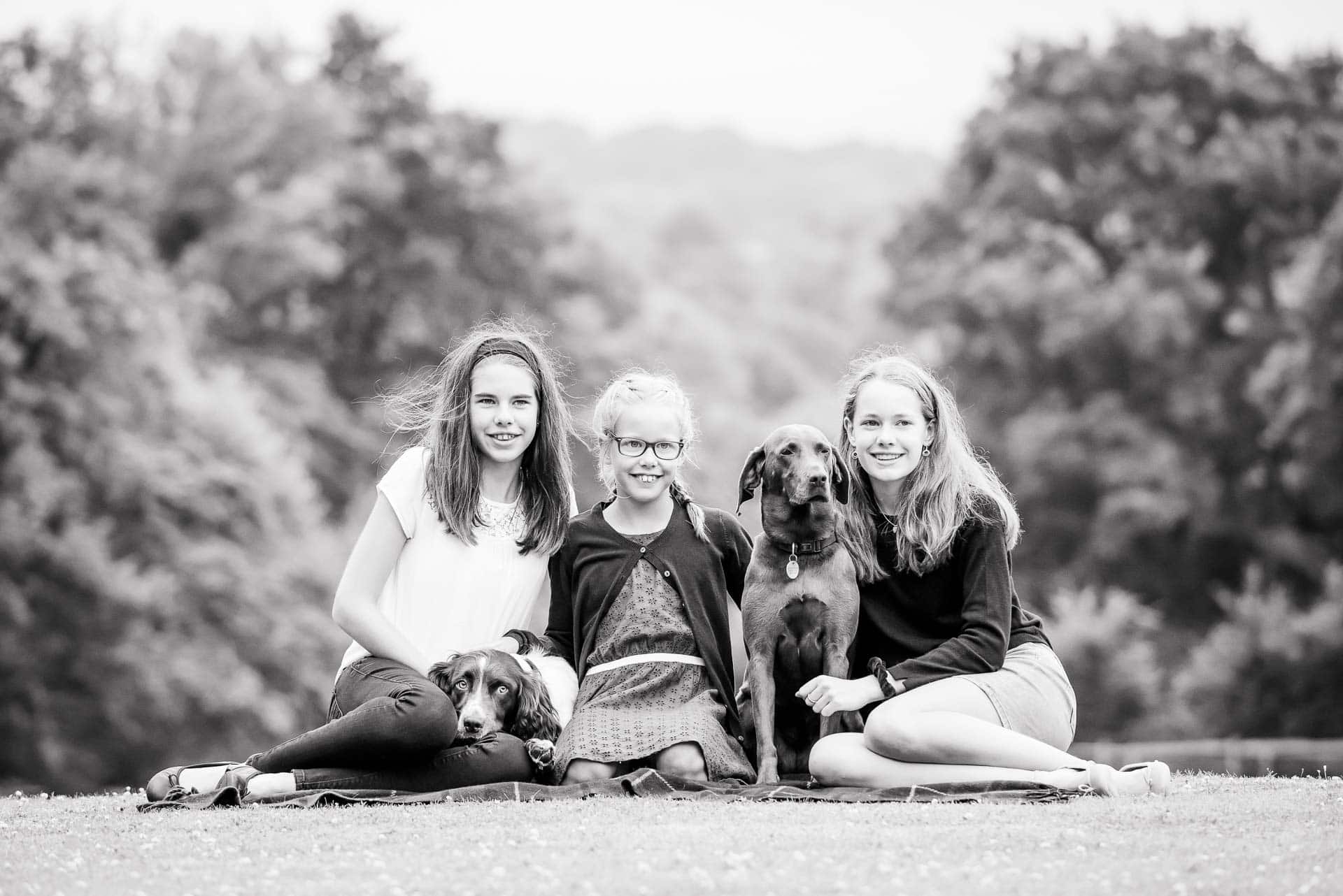 Black and white portrait of 3 sisters sitting on a lawn during their family photoshoot in Sussex