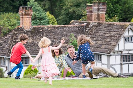 3 children running towards their parents who are sitting down on the lawn outside their house during their family photoshoot in Sussex