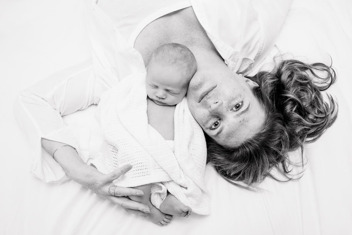 black and white picture of a mother and newborn baby laying on bed