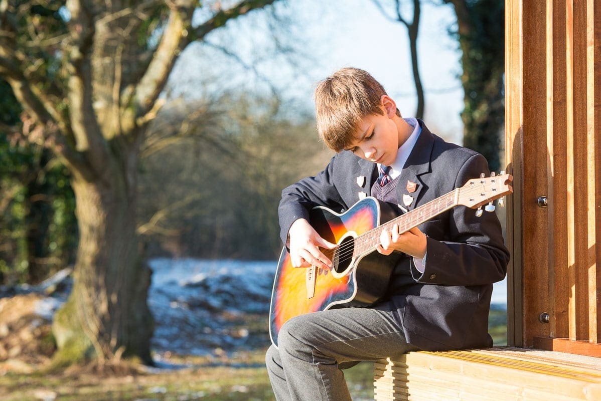 Boy sitting outside playing his guitar, photographed by school marketing photographer in Sussex