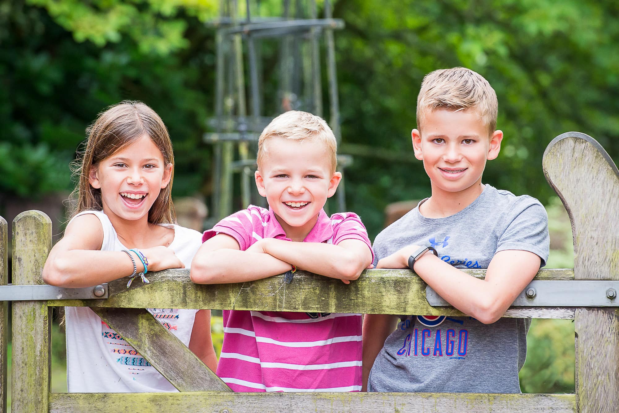 Three siblings wearing brightly coloured clothes leaning on a gate
