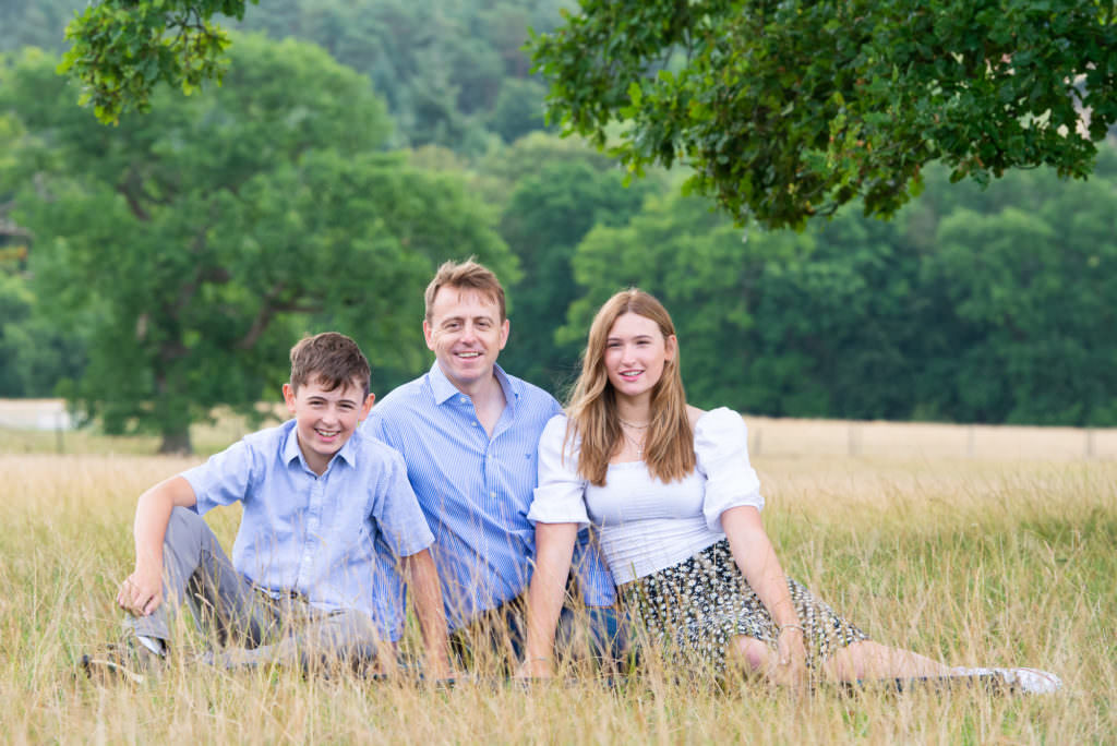 Father sitting in the grass with his two children during a Worth Abbey Family Photoshoot