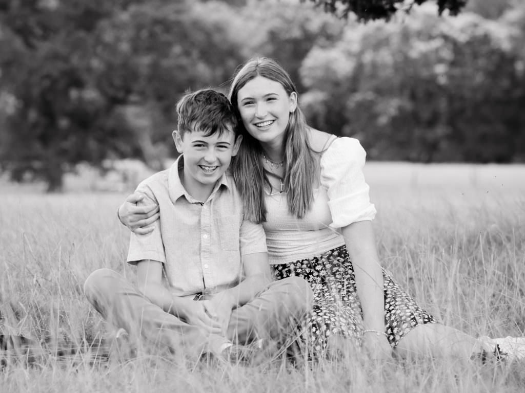 Brother and sister sitting in a grass meadow during a Worth Abbey family photoshoot in Sussex