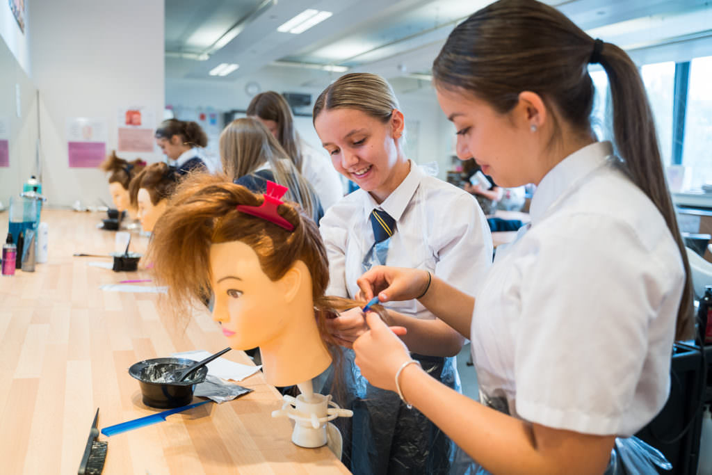 School girls practising their hairdressing skills on a manikin