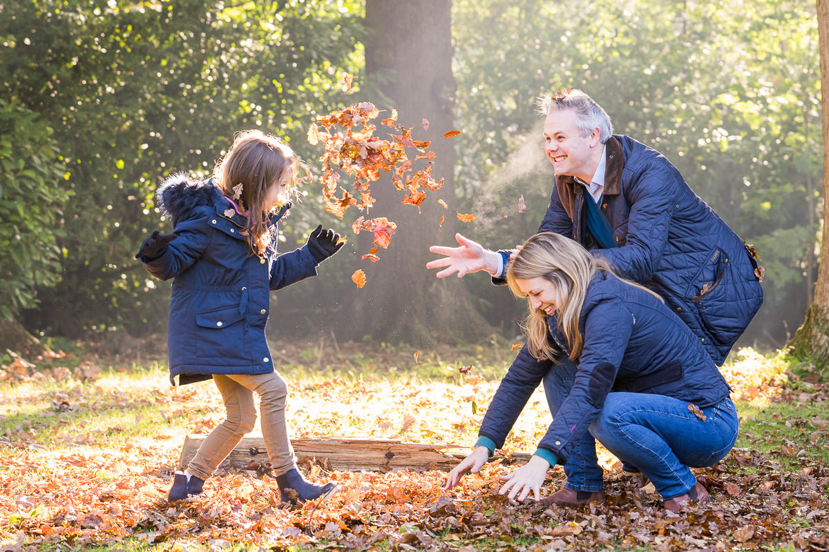 Mother and father throwing leaves with their daughter during their autumn family photoshoot in Sussex