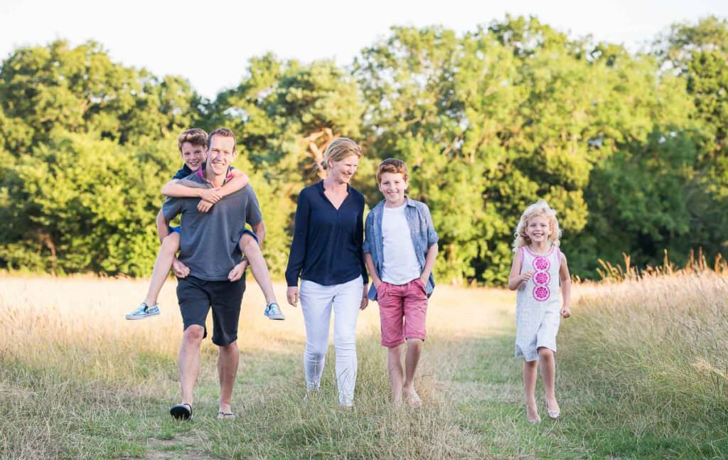 Parents and their 3 children walking through a grass field during their Family Photoshoot in Ardingly