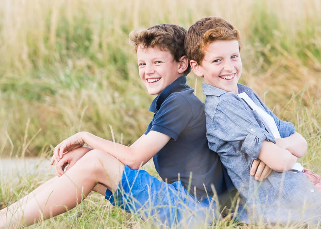 Two brothers wearing blue sitting back to back and smiling at the camera during their Family Photoshoot in Ardingly, West Sussex