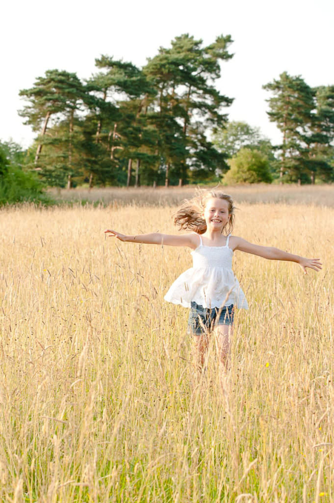 A young girl running through long golden grass during her family photoshoot in Ardingly