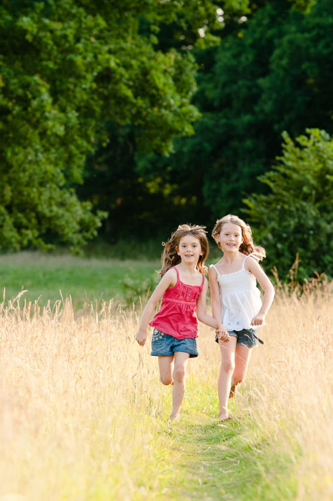 Two sisters running along a grass path during their summer family photoshoot in Ardingly