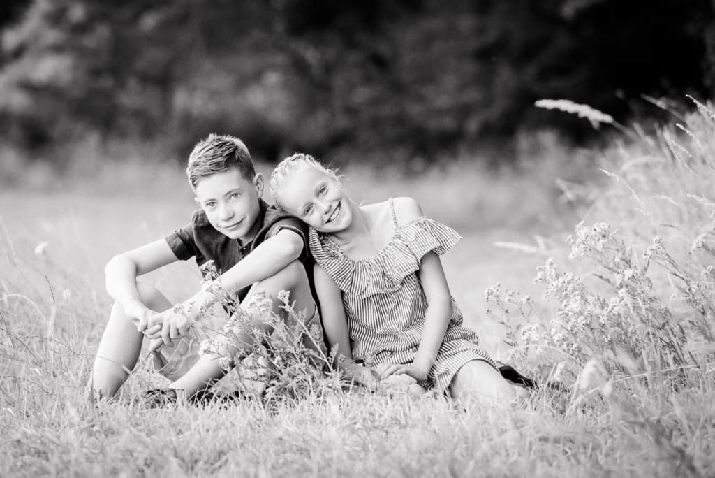 Black and white image of two children snuggling up together in a meadow during their family photoshoot in Ardingly