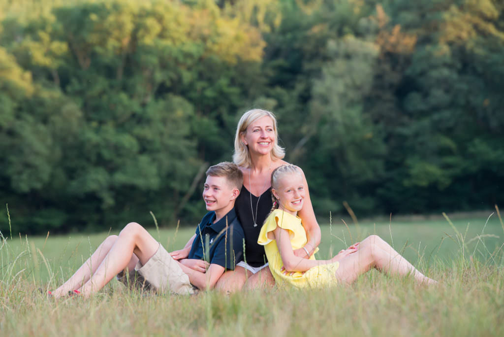 A mum and her two children sitting in long grass, photographed during their Family Photoshoot in Ardingly