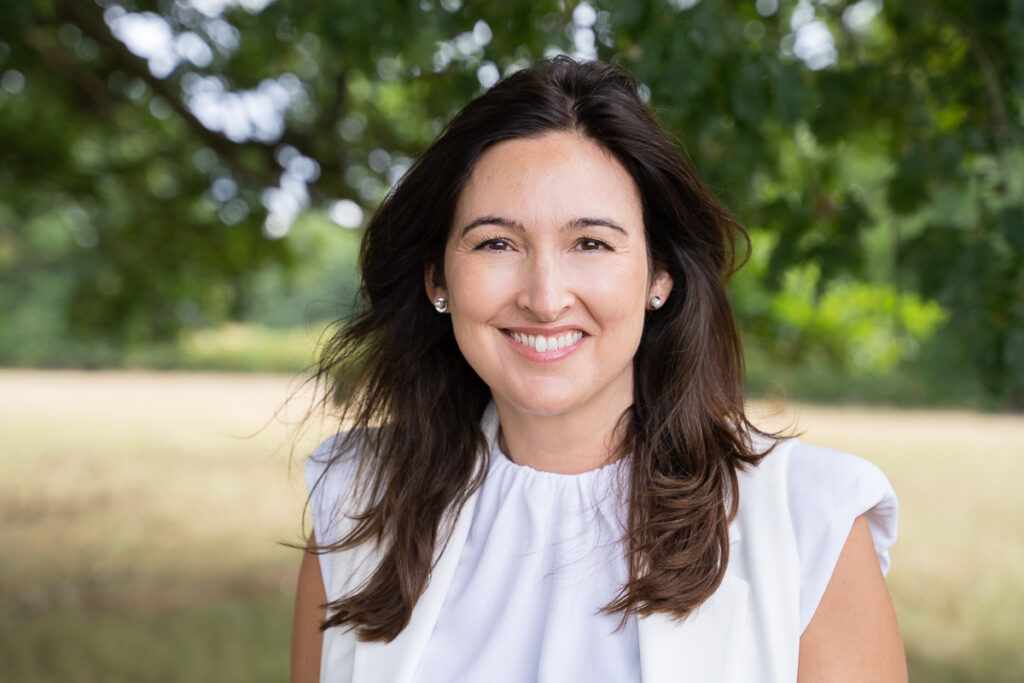 Relaxed outdoor headshot of a businesswoman wearing a white top taken under a tree during the summer in Sussex